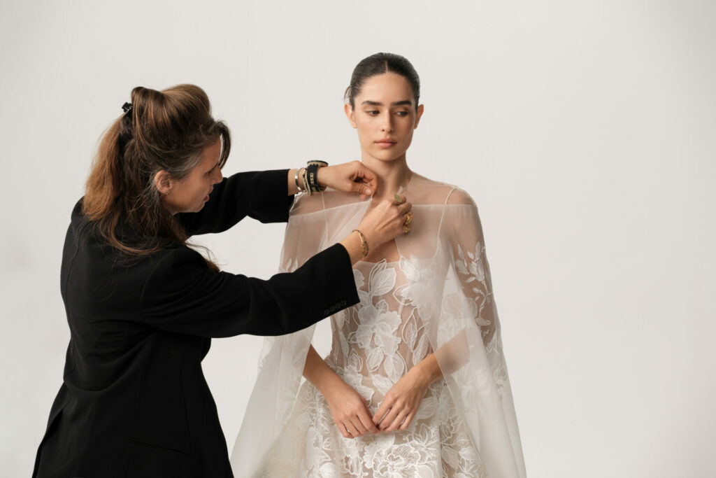 Woman fixes bride’s veil on white background.