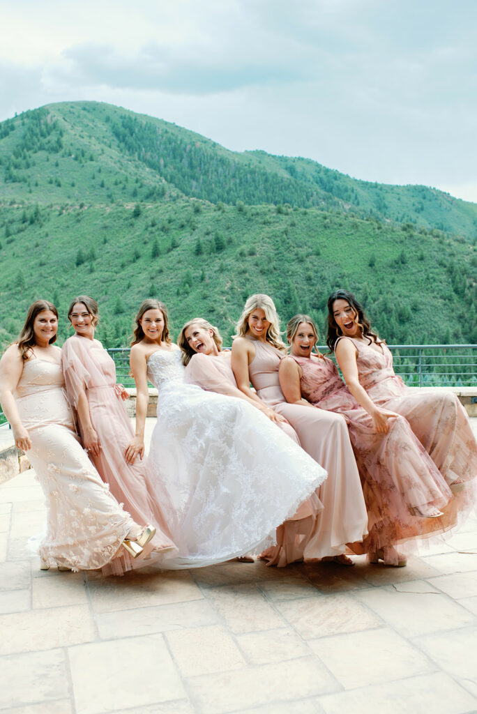 Six women in pink and white dresses pose playfully outdoors.