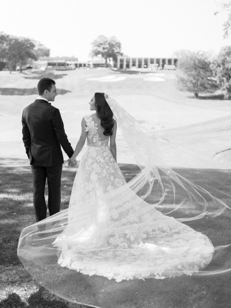 Bride and groom hold hands outdoors in sunlight.