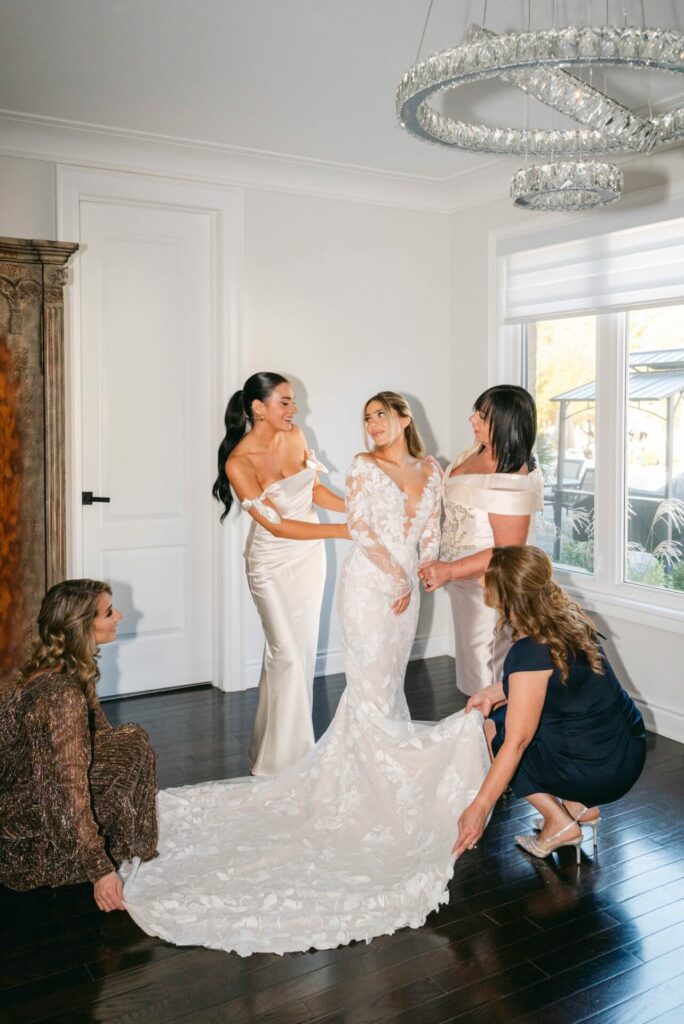 Bride smiling as women adjust her SS2026 dress.