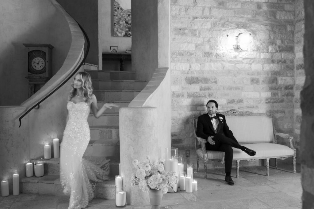 Bride descends candle-lit stairs; groom watches in vintage room.