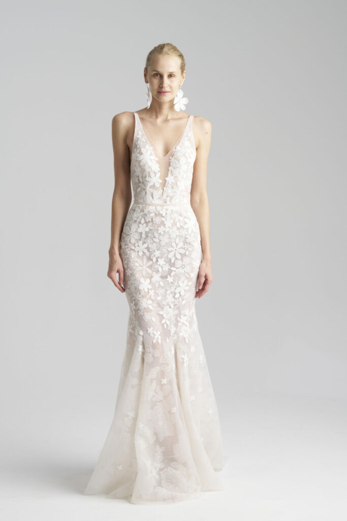 Woman in white floral lace gown, slicked-back hair.