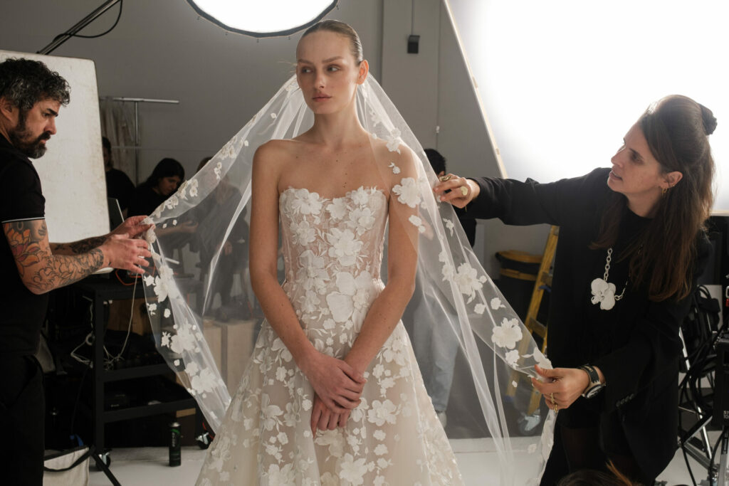 Bride in lace dress gets veil adjusted in studio.