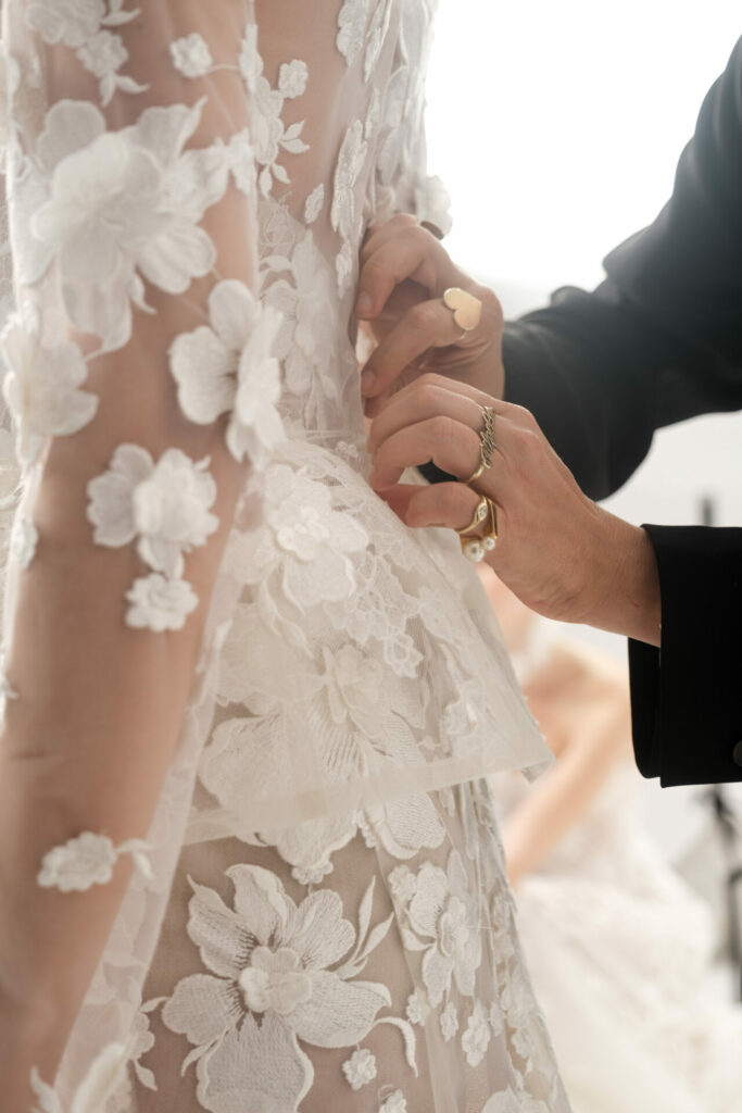 Hands adjusting waist of sheer white floral gown.