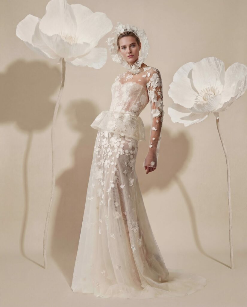 Woman in sheer floral gown stands between giant paper flowers.