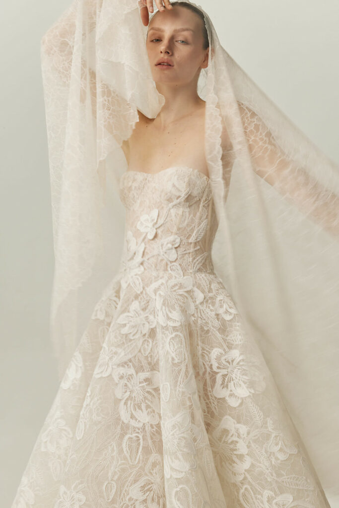 Woman in strapless lace wedding gown holds sheer veil.