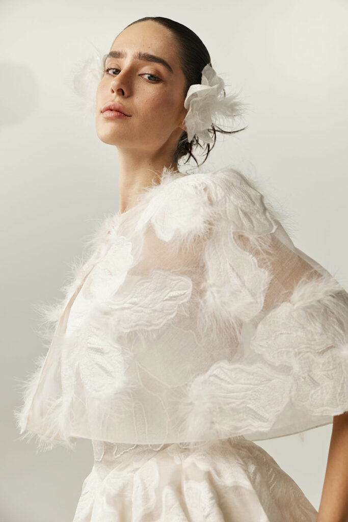 Woman in sheer feathered white cape and dress.