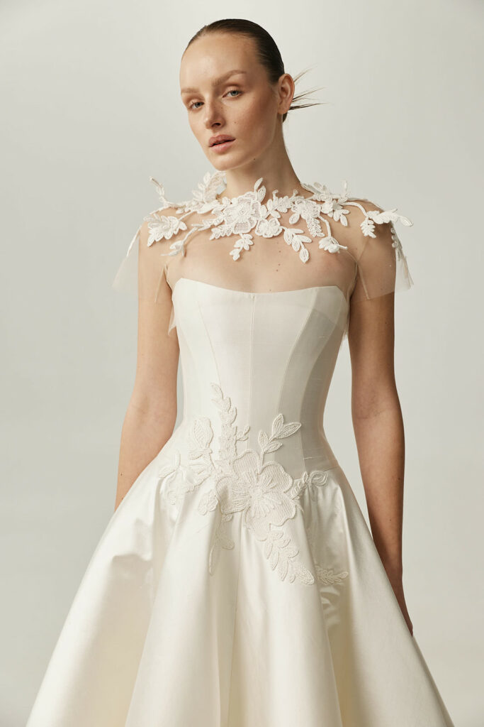 Woman in strapless white embroidered gown, plain background.