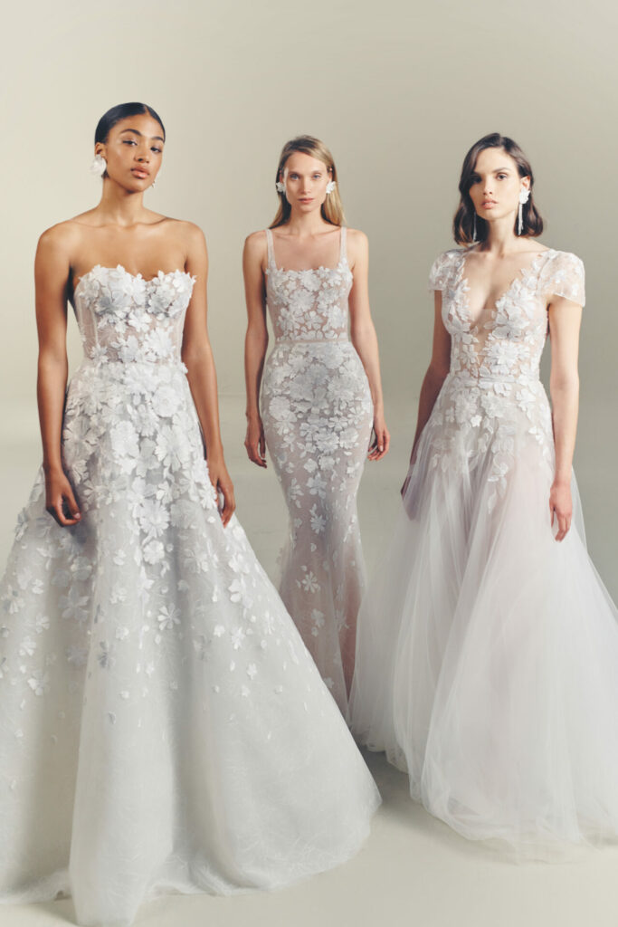 Three women pose in light floral wedding gowns.