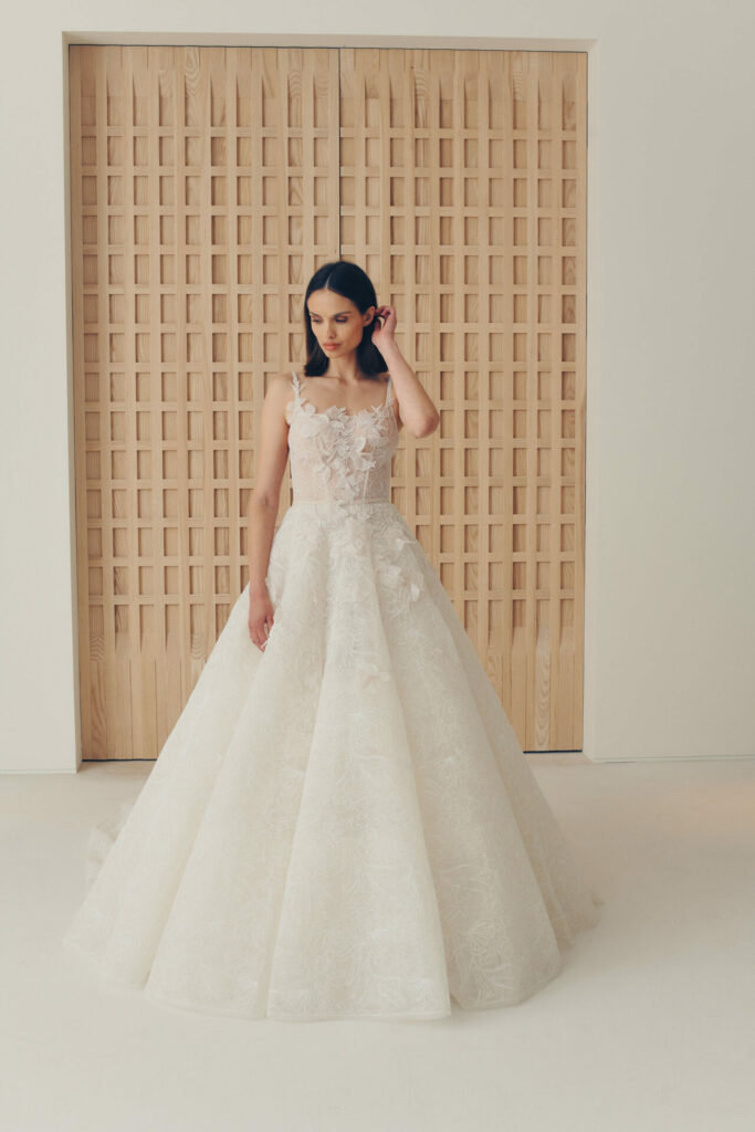 Woman in white floral ballgown poses by lattice wall.