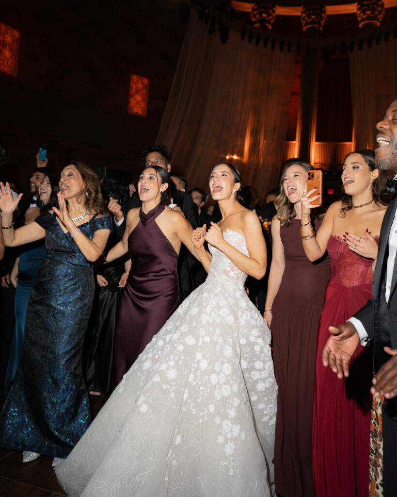 Bride in white floral gown celebrates with joyful guests.