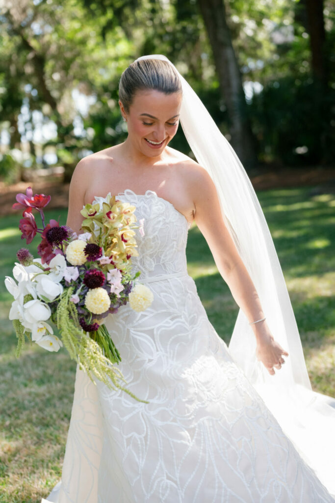 Bride in white SS2026 gown, smiling with bouquet outdoors.