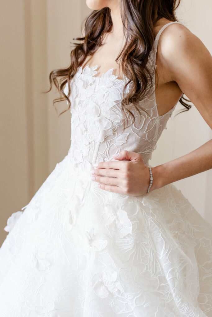 Woman in floral lace gown, wavy hair, bracelet.