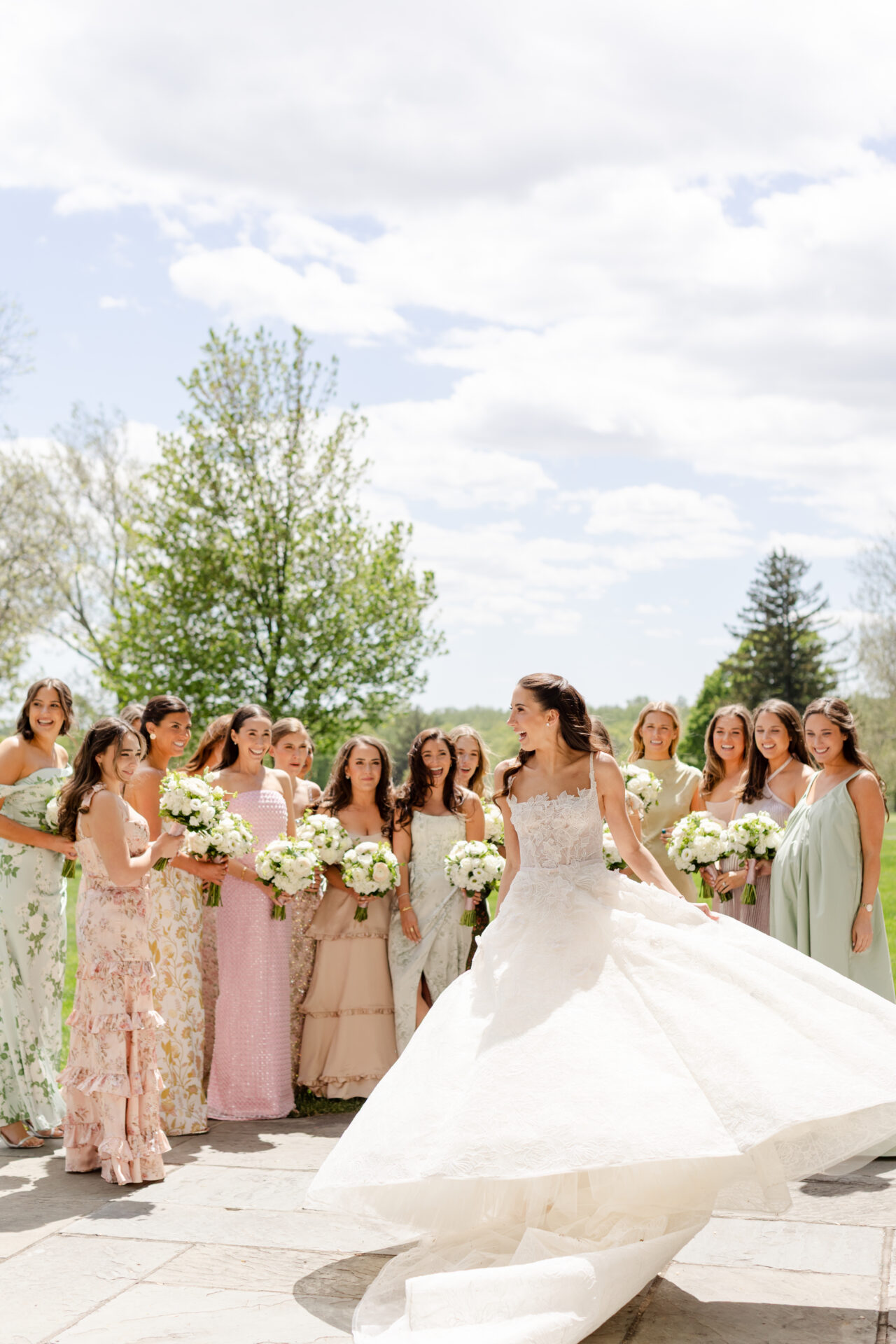 Bride twirls outdoors with pastel-dressed bridesmaids, bouquets.