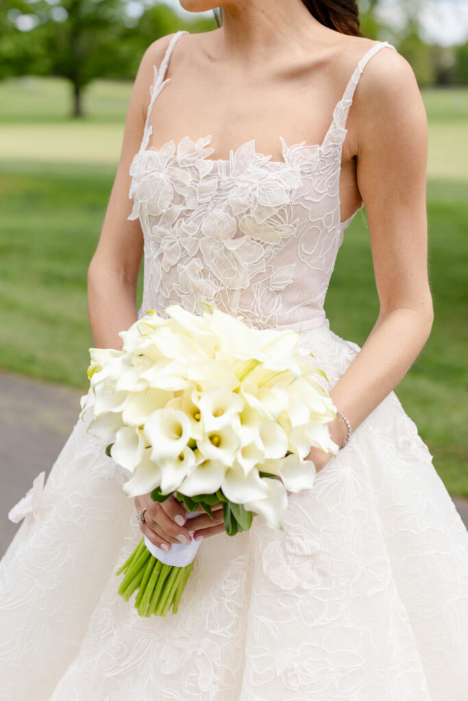 Bride in lace gown with calla lilies, outdoors.