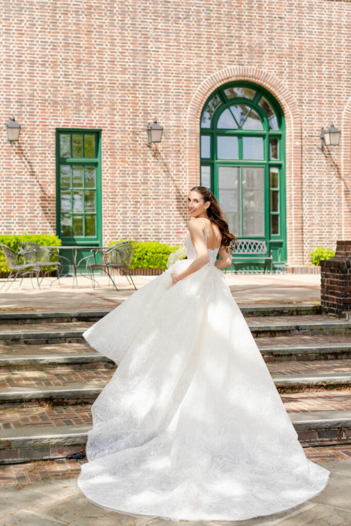Bride in flowing couture gown smiles on steps.