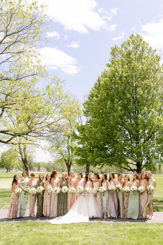 Bride in couture gown with bridesmaids outdoors, bouquets in hand.