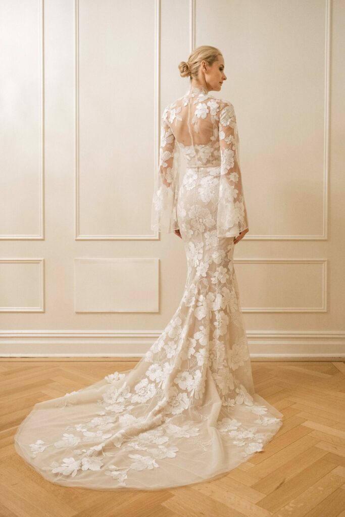Woman in a white lace wedding gown faces wall.