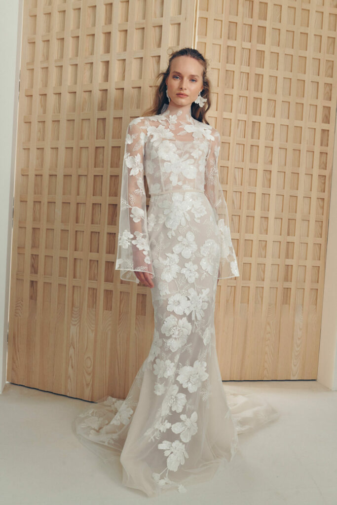 Woman in sheer white lace gown before wood panel.