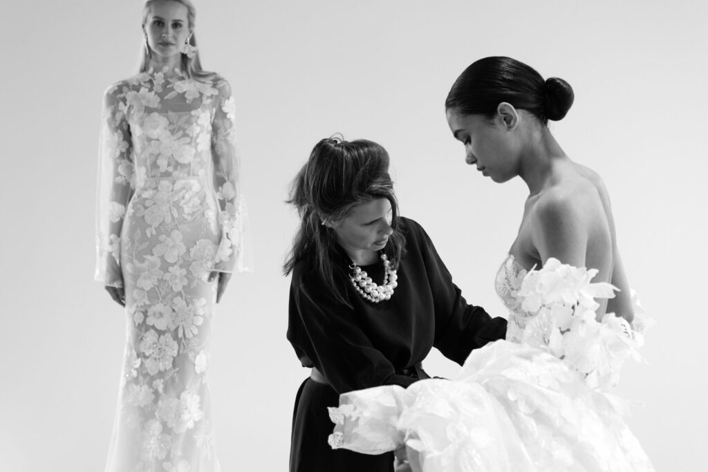 Designer adjusts lace gown; models pose in studio.