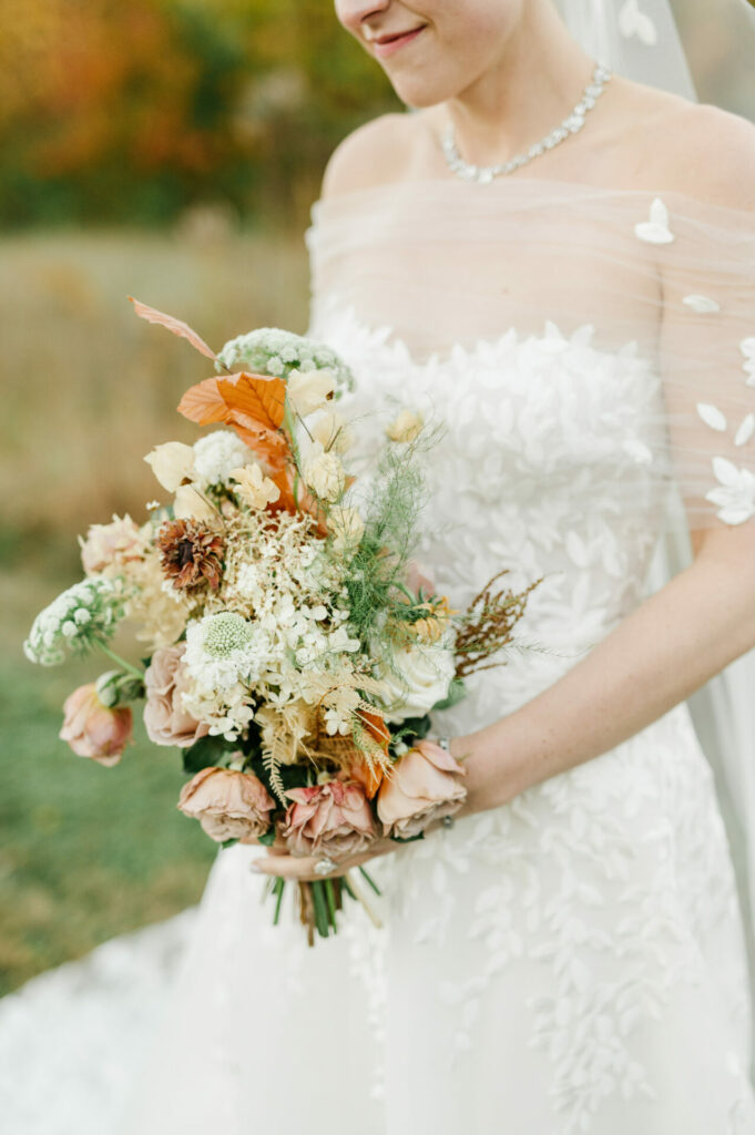 Bride in white lace dress with rustic bouquet outdoors.