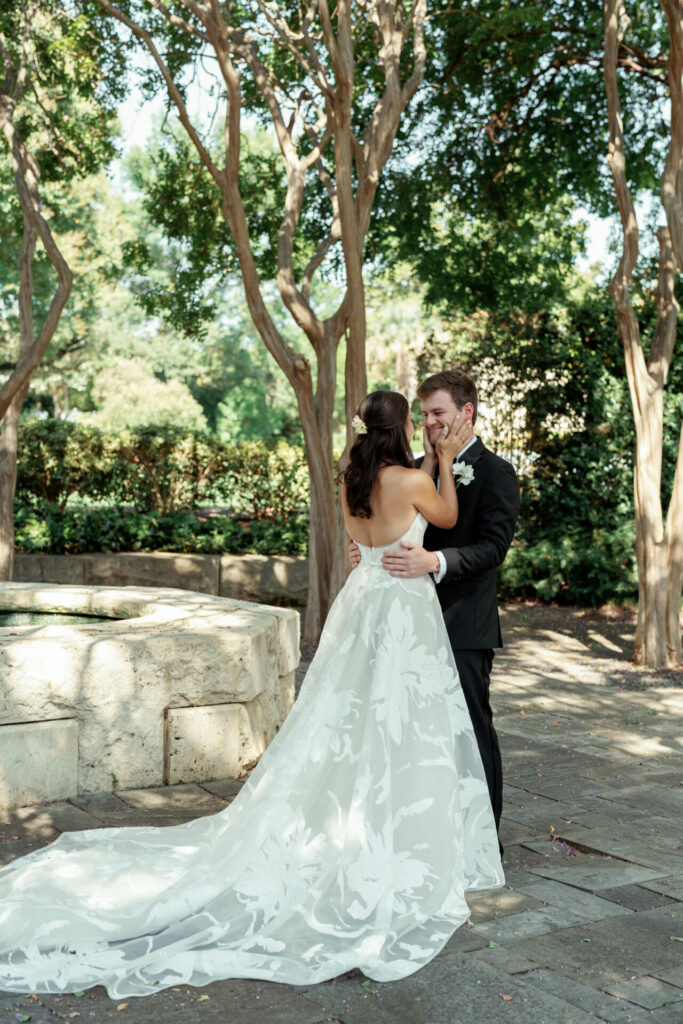 Bride in strapless gown embraces groom in sunlit garden.