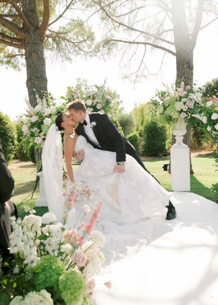 Bride and groom kiss in lush, floral outdoor setting.