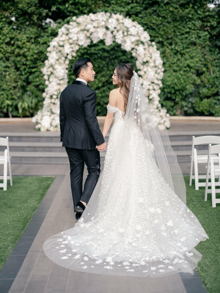 Smiling bride and groom walk hand-in-hand outdoors.