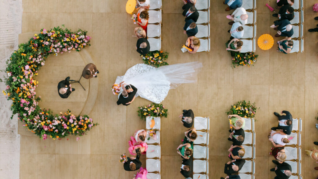 Katya Ruiz walks aisle in luxe gown, grand floral arch.
