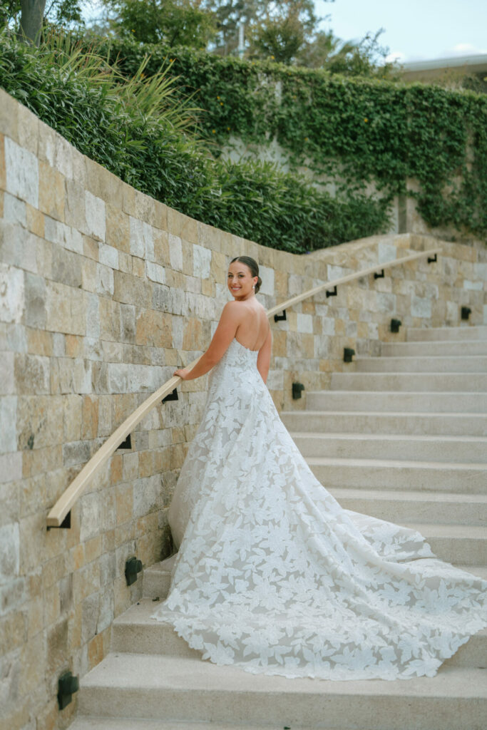 Bride in strapless white gown smiles on stone steps.
