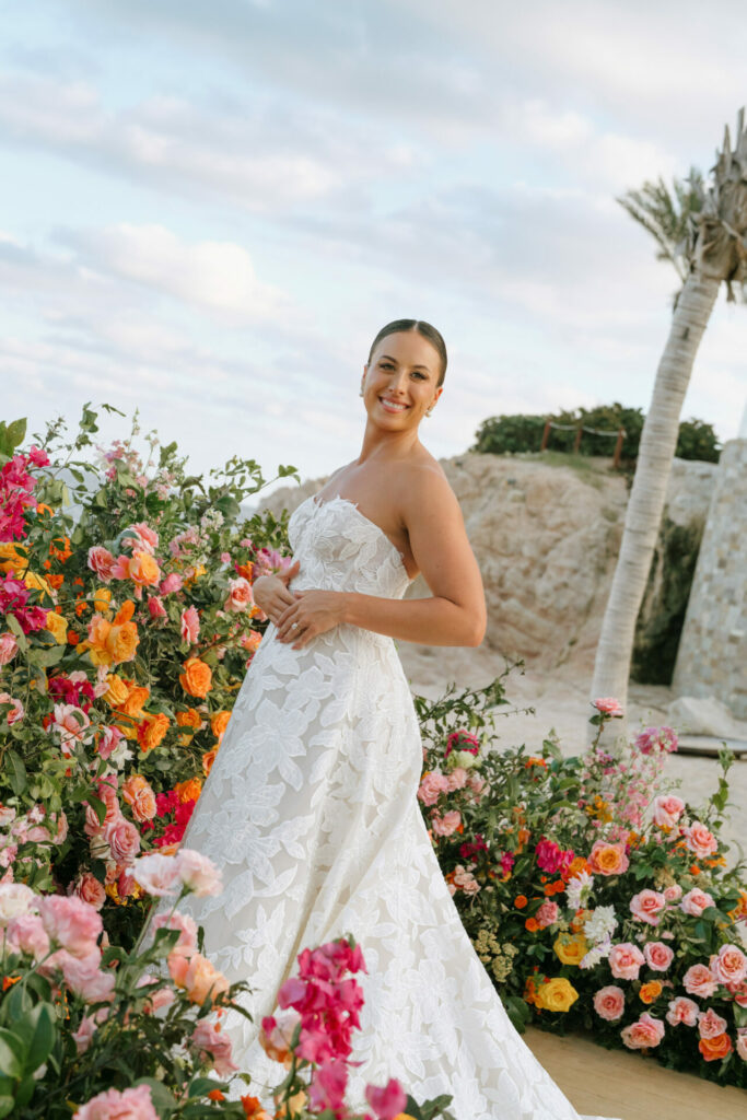 Katya Ruiz in strapless floral gown among colorful flowers outdoors.