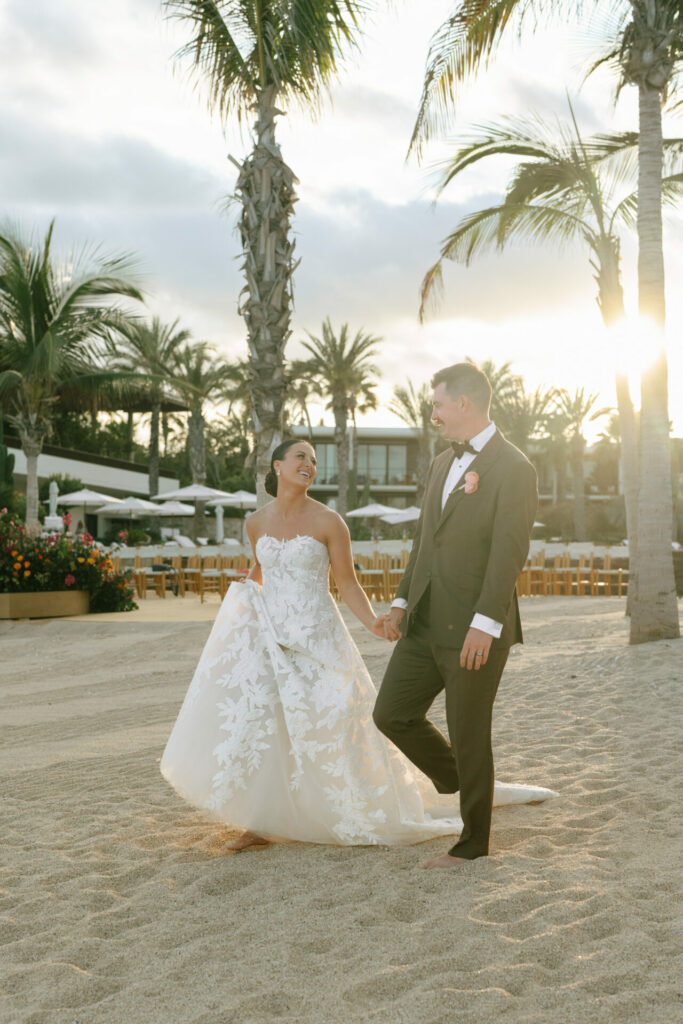 Bride and groom barefoot on beach at sunset.