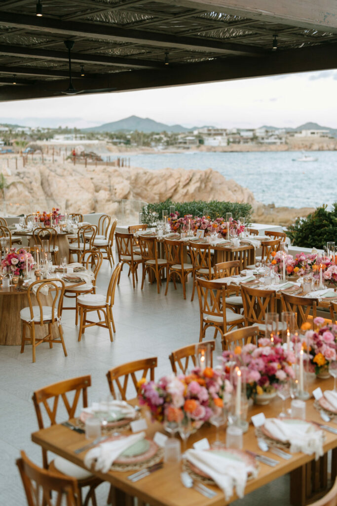 Chic outdoor tables, vivid florals, candles, ocean cliff view.