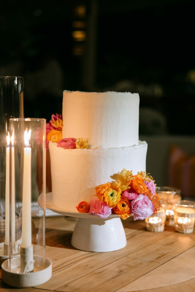 White cake with colorful flowers, surrounded by candles.