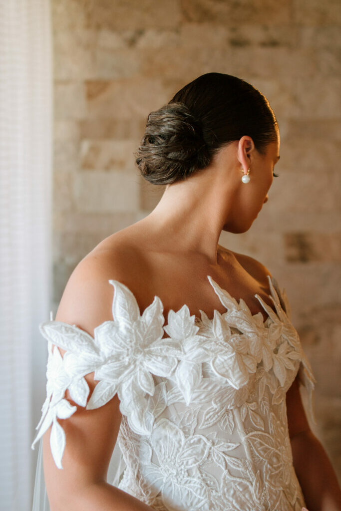 Woman in floral-appliqué white lace gown, elegant bridal style.