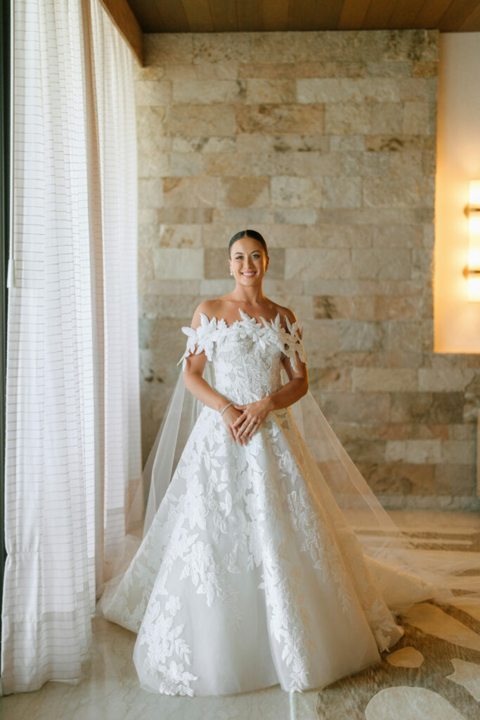 Bride in lace Mira Zwillinger gown, smiling indoors.