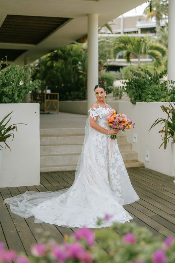 Bride in white gown with bouquet on wooden deck.