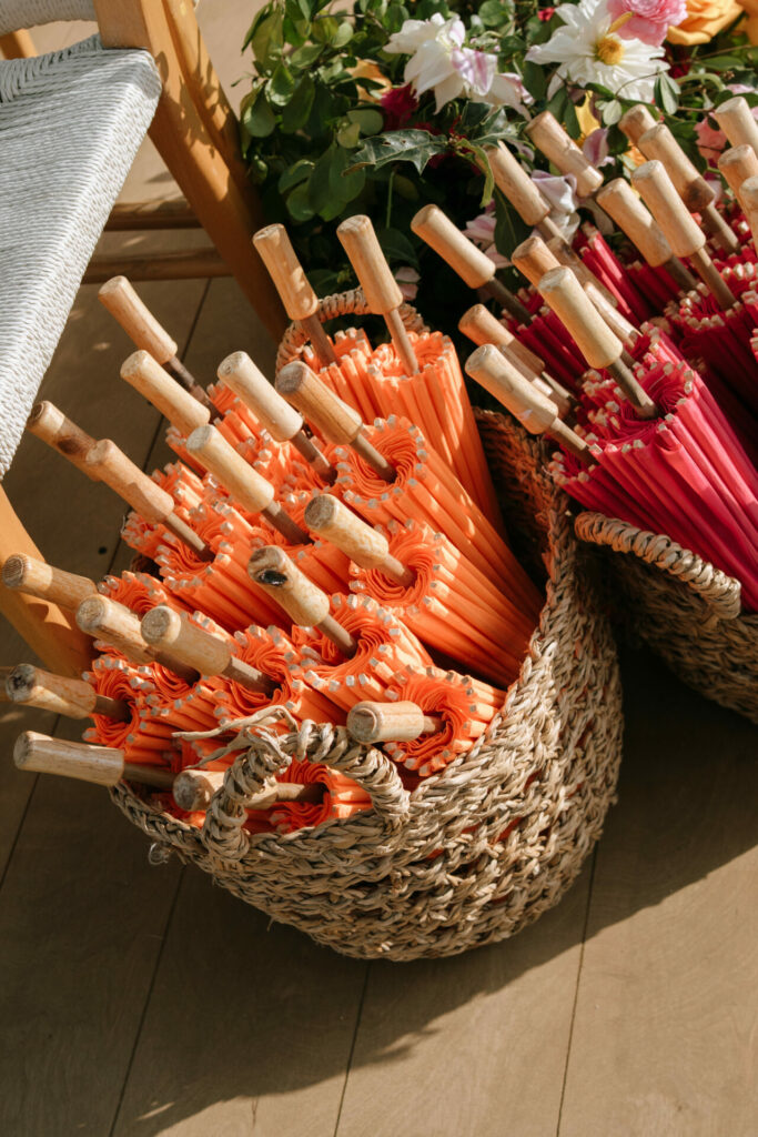 Baskets of orange and pink parasols, chair, flowers nearby.