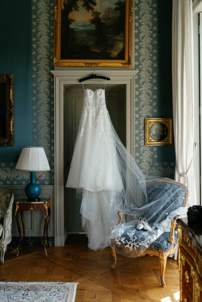 Bridal couture gown on door, shoes on veiled chair.