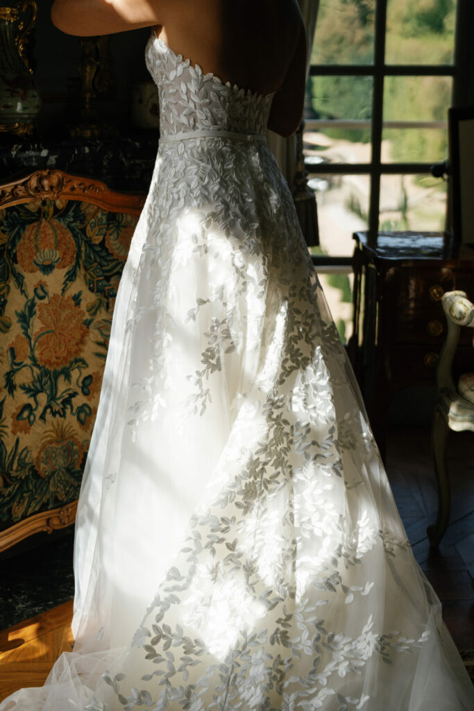 Person in floral white Mira Zwillinger gown by window.