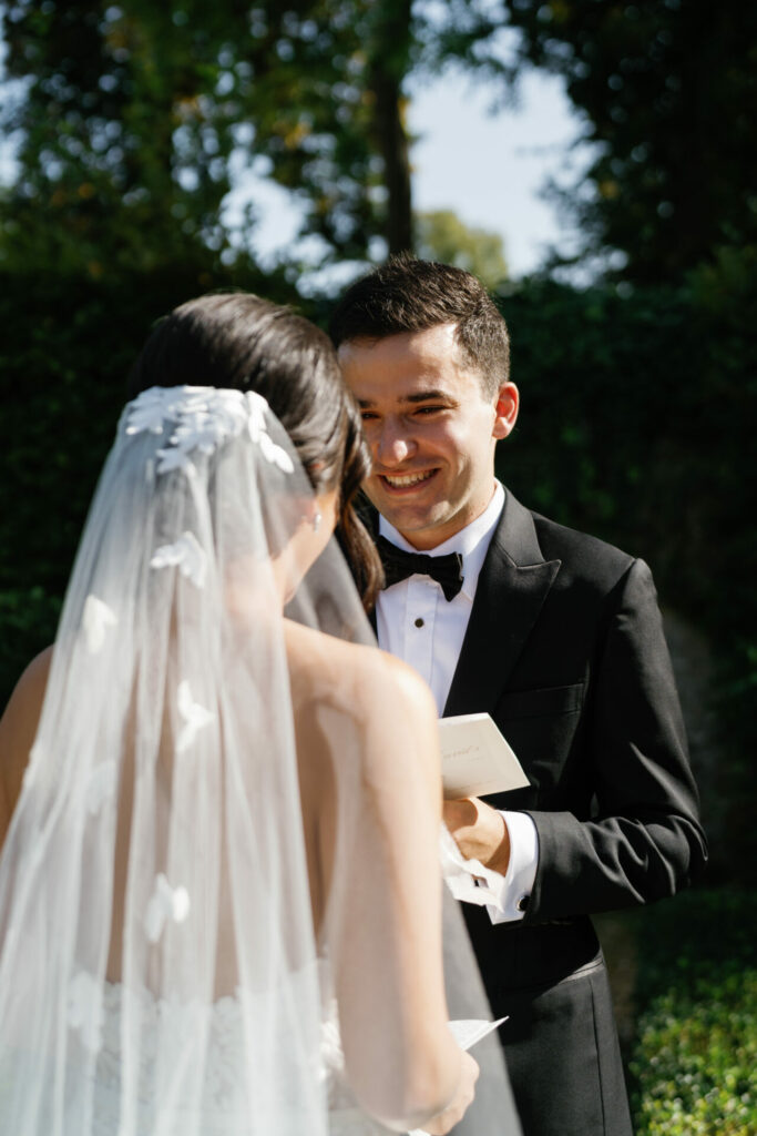 Smiling groom watches Katya Ruiz exchange vows outdoors.