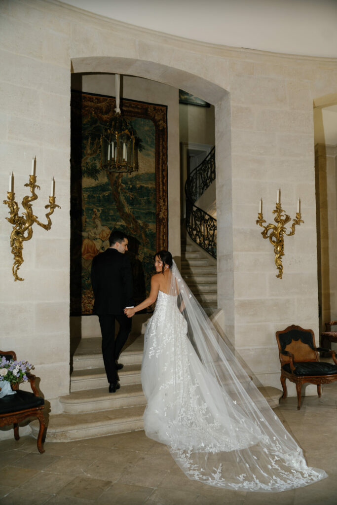 Bride and groom ascend stone stairs in luxury venue.