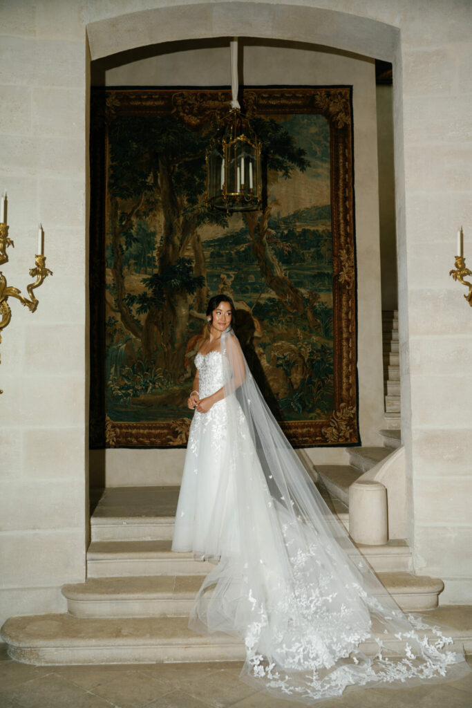Katya Ruiz in couture gown, long veil on stone steps.