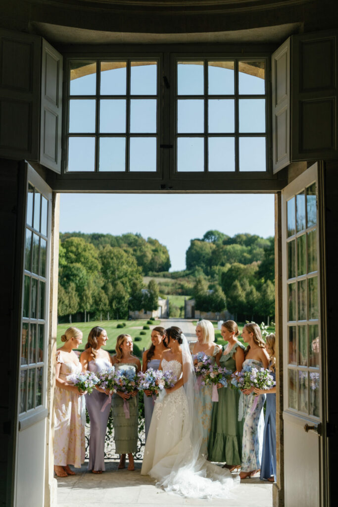 Bride and seven bridesmaids with bouquets by open doors.