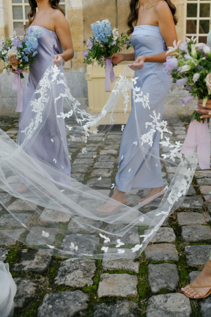 Bridesmaids in blue help carry floral-embroidered wedding veil.