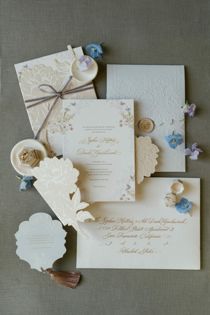 Elegant wedding stationery, rings, and flowers on gray.