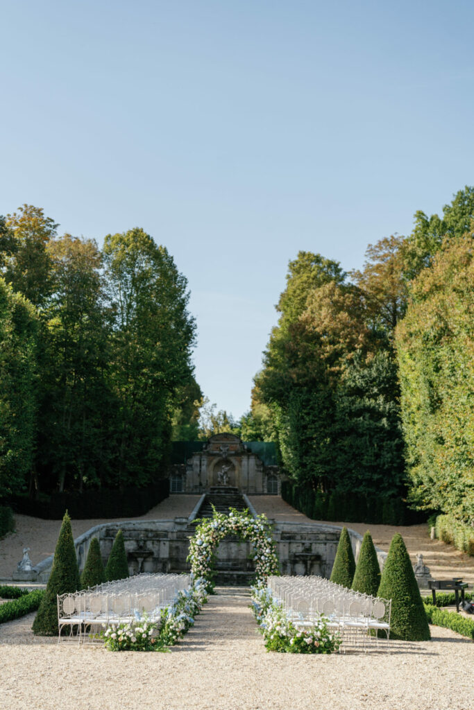 Elegant outdoor wedding setup with white chairs, floral arch.