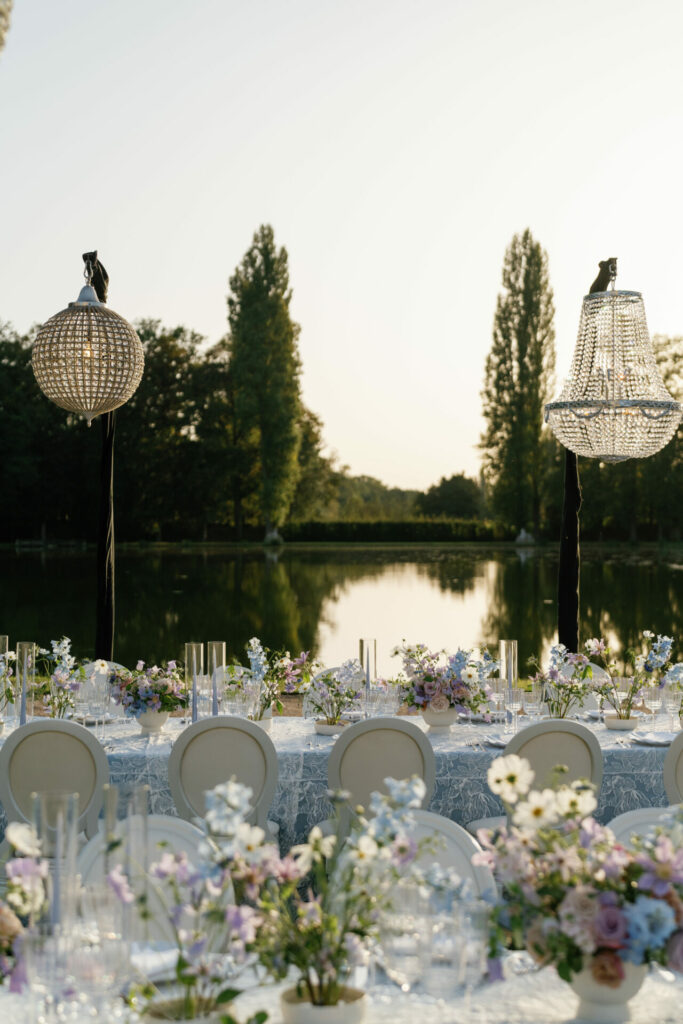 Chic lakeside table, floral centerpieces, chandeliers at sunset.