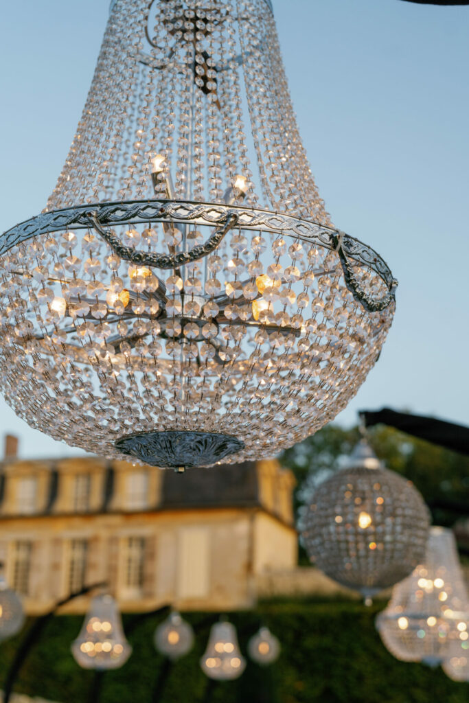 Crystal chandeliers glow at dusk before historic building.