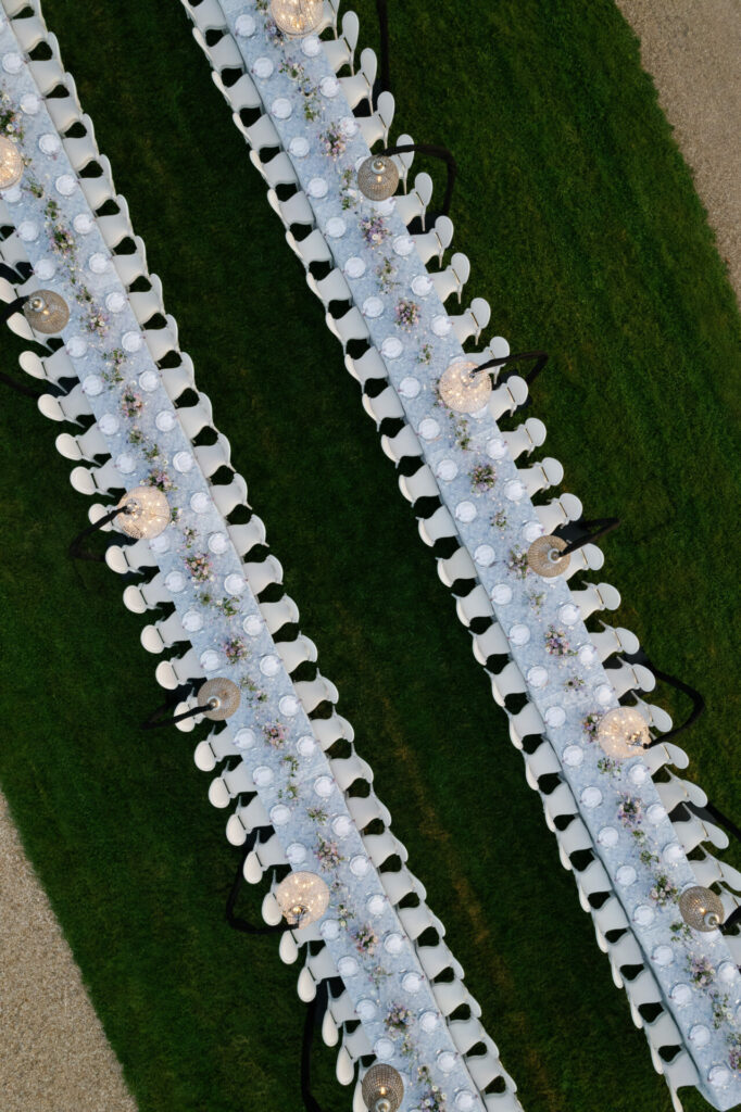 Two elegant banquet tables with white chairs on grass.